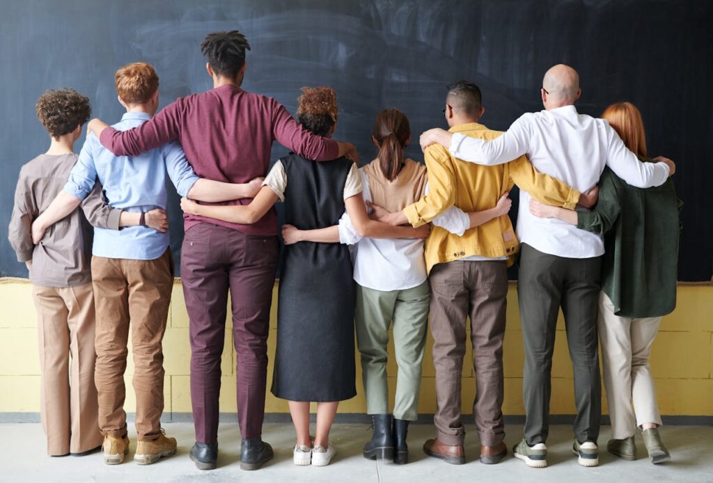 A group of people standing  indoors in front of a blank blackboard